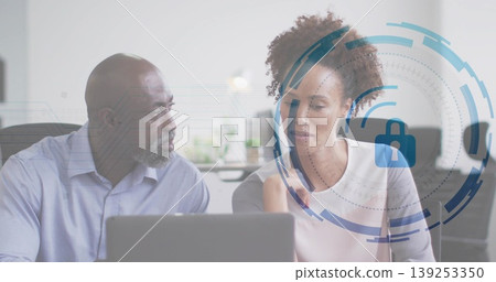 Colleagues reviewing cybersecurity interface at desk in office, with digital lock overlay on laptop Colleagues reviewing cybersecurity interface at desk in office, with digital lock overlay on laptop 139253350