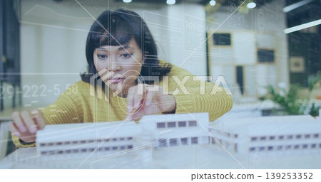 Leaning Asian woman in yellow sweater adjusting white scale model in studio, with digital overlays Leaning Asian woman in yellow sweater adjusting white scale model in studio, with digital overlays 139253352