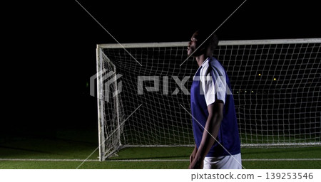 Anticipating player wearing blue vest shorts shoes on turf under floodlights, goal net, copy space Anticipating player wearing blue vest shorts shoes on turf under floodlights, goal net, copy space 139253546