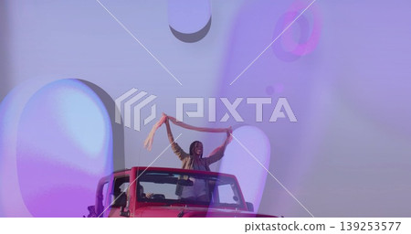 Driving red convertible carrying two friends on open road, with flowing scarf and sunglasses 139253577