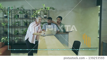 Leaning professional wearing light pink blazer pointing at laptop in office, with team amid plants Leaning professional wearing light pink blazer pointing at laptop in office, with team amid plants 139253593