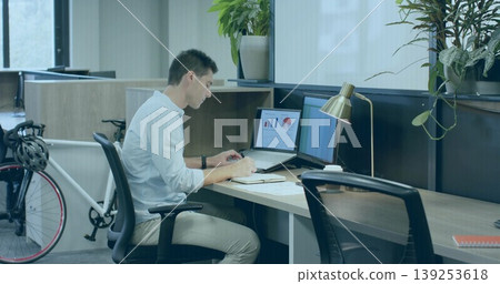 Writing office worker jotting notes at modern coworking desk, with laptop notebook monitor bicycle Writing office worker jotting notes at modern coworking desk, with laptop notebook monitor bicycle 139253618