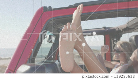 Soaking up sunshine, two friends wearing sunglasses cruising in red open-top SUV by sandy beach 139253638