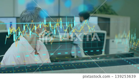 Woman wearing pink button-down shirt analyzing holographic data at office desk, with dual monitors 139253639