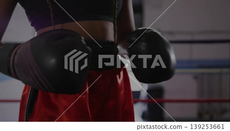Posing boxer wearing black sports bra red boxing shorts holding gloves in boxing ring Posing boxer wearing black sports bra red boxing shorts holding gloves in boxing ring 139253661