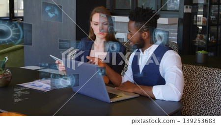 Reviewing data two business professionals pointing at laptop and tablet in office, with holograms Reviewing data two business professionals pointing at laptop and tablet in office, with holograms 139253683