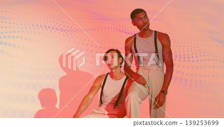 Posing male models wearing tank tops, suspenders and beige pants in studio, with gradient backdrop Posing male models wearing tank tops, suspenders and beige pants in studio, with gradient backdrop 139253699