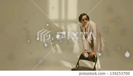 Man in beige suit leaning on black folding chair in studio, sunglasses, light spots, copy space Man in beige suit leaning on black folding chair in studio, sunglasses, light spots, copy space 139253700