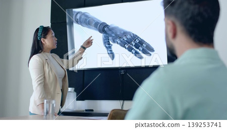 Pointing blazer-clad woman presenter to robotic prosthetic hand display in meeting room, copy space 139253741