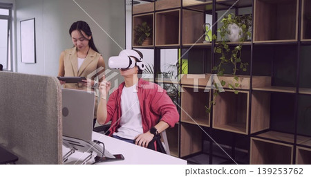 Man in red overshirt testing virtual reality headset at office desk, with tablet laptop shelf Man in red overshirt testing virtual reality headset at office desk, with tablet laptop shelf 139253762