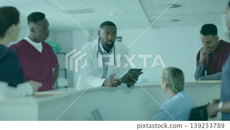 Speaking Black male doctor holding tablet while collaborating at nursing station, with monitors 139253789