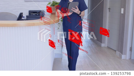 Standing receptionist wearing scrubs behind curved desk in clinic hallway, displaying digital UI 139253798