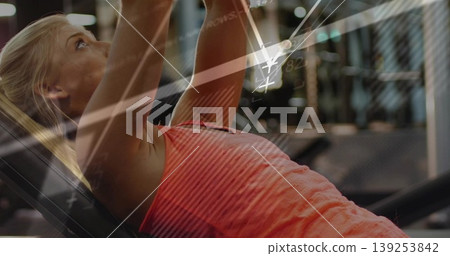 Pressing dumbbells overhead woman wearing orange tank top and leggings in gym, with data overlay Pressing dumbbells overhead woman wearing orange tank top and leggings in gym, with data overlay 139253842