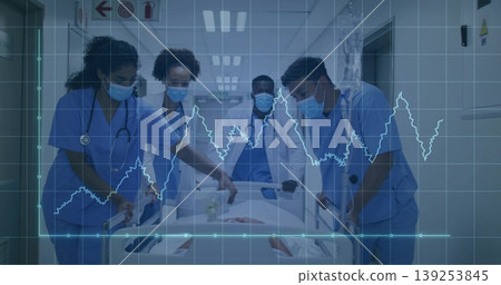 Medical team wearing masks and stethoscopes pushing patient on gurney down ward corridor with ECG Medical team wearing masks and stethoscopes pushing patient on gurney down ward corridor with ECG 139253845