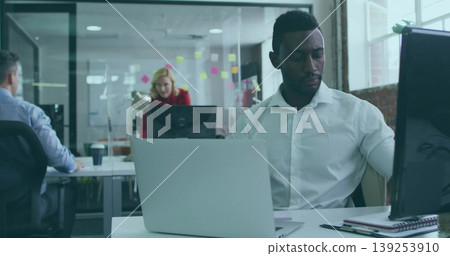 African American man working on laptop and adjusting monitor in open-plan office, with coffee cup African American man working on laptop and adjusting monitor in open-plan office, with coffee cup 139253910