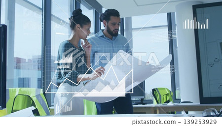 Two architects examining blueprint in modern office with mesh chairs, monitors and digital graphs Two architects examining blueprint in modern office with mesh chairs, monitors and digital graphs 139253929