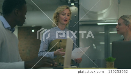 Presenting White woman in office attire showing charts in meeting area, with laptops, coffee mug Presenting White woman in office attire showing charts in meeting area, with laptops, coffee mug 139253962