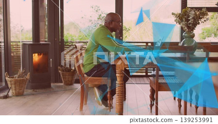 Working man wearing green pullover typing on laptop on table in sunlit room, with wood stove Working man wearing green pullover typing on laptop on table in sunlit room, with wood stove 139253991