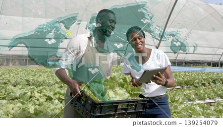 Two farm workers monitoring lettuce trays in greenhouse, holding crate and tablet with map overlay Two farm workers monitoring lettuce trays in greenhouse, holding crate and tablet with map overlay 139254079