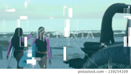 Walking surfers in pink rash guards with surfboards along shoreline, with bicycle wheel, metal rack 139254109