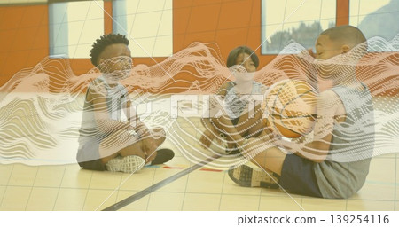Sitting cross-legged children wearing sportswear on gym court, holding basketball near court lines Sitting cross-legged children wearing sportswear on gym court, holding basketball near court lines 139254116