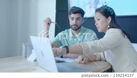 Collaborating woman and man examining laptop and tablet at office meeting table, with stylus papers Collaborating woman and man examining laptop and tablet at office meeting table, with stylus papers 139254137
