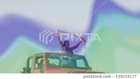 Woman standing through open roof of red Jeep Wrangler in pastel gradient hills, with scarf flying Woman standing through open roof of red Jeep Wrangler in pastel gradient hills, with scarf flying 139254177