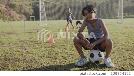 Squatting boy in sportswear training on soccer field with training cones and goal net, copy space Squatting boy in sportswear training on soccer field with training cones and goal net, copy space 139254192