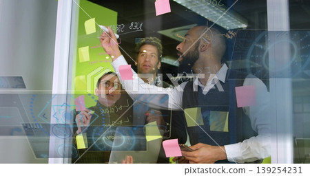 Brainstorming colleagues discussing ideas on glass wall at office, with tablet and sticky notes Brainstorming colleagues discussing ideas on glass wall at office, with tablet and sticky notes 139254231
