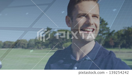 Smiling man wearing navy polo shirt standing on sunlit golf fairway with grid overlay, copy space 139254242