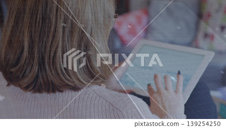 Holding touchscreen tablet and browsing apps while sitting on sofa in living room, wearing sweater Holding touchscreen tablet and browsing apps while sitting on sofa in living room, wearing sweater 139254250