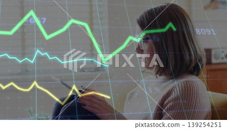 Interacting woman holding tablet, tracing graph overlays on window blinds in lounge, copy space Interacting woman holding tablet, tracing graph overlays on window blinds in lounge, copy space 139254251