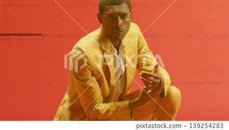 Posing mid adult model in yellow tailored suit and white shirt crouching in studio, glitch backdrop Posing mid adult model in yellow tailored suit and white shirt crouching in studio, glitch backdrop 139254283
