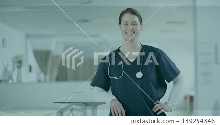 Smiling nurse in navy scrubs leaning on table in hospital corridor, with stethoscope, patient beds Smiling nurse in navy scrubs leaning on table in hospital corridor, with stethoscope, patient beds 139254346