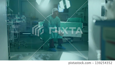 Leaning surgeon clasping hands on stool in scrubs in OR, with surgical lights and monitors Leaning surgeon clasping hands on stool in scrubs in OR, with surgical lights and monitors 139254352
