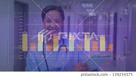 Smiling nurse in blue scrubs with stethoscope reviewing data on clipboard pen in hospital corridor 139254375