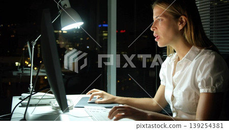 Typing office worker wearing white blouse using computer in office at night, ashtray, copy space Typing office worker wearing white blouse using computer in office at night, ashtray, copy space 139254381