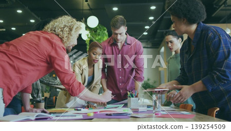 Leaning six professionals pointing at colorful papers on wooden table in open office, with markers Leaning six professionals pointing at colorful papers on wooden table in open office, with markers 139254509