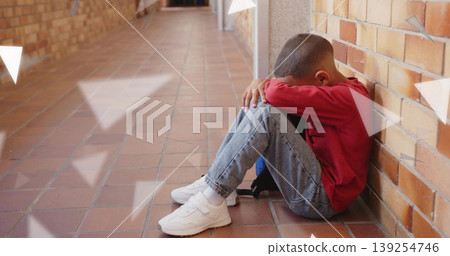 Boy wearing red shirt hugging knees against brick wall in school hallway, with backpack, copy space Boy wearing red shirt hugging knees against brick wall in school hallway, with backpack, copy space 139254746