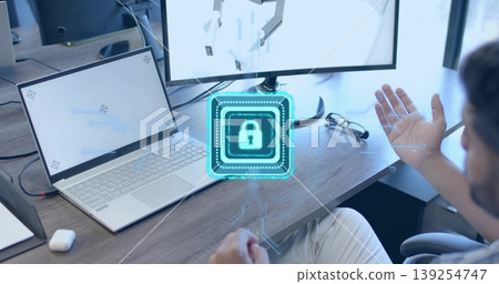 Gesturing man in shirt touching holographic lock icon above desk, with laptop, monitor, copy space 139254747