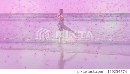 Balancing woman in short floral dress lifting leg in shallow beach water, with pink dot overlay Balancing woman in short floral dress lifting leg in shallow beach water, with pink dot overlay 139254774