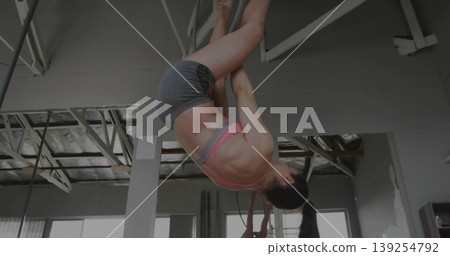Inverting fitness dancer wearing pink sports bra gripping pole in studio, with large windows 139254792