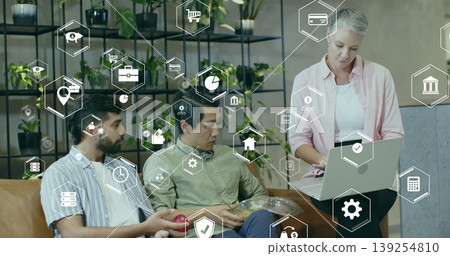 Three professionals reviewing printed charts on laptop in office lounge, with digital finance icons Three professionals reviewing printed charts on laptop in office lounge, with digital finance icons 139254810