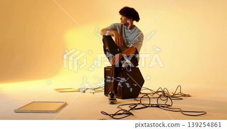 Sitting man wearing t-shirt, earphones on black amplifier at studio, surrounded by audio cables Sitting man wearing t-shirt, earphones on black amplifier at studio, surrounded by audio cables 139254861