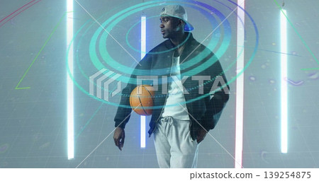 Posing male athlete in sportswear holding orange basketball in tech studio, with hologram rings 139254875