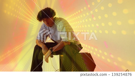 Musician sitting on amplifier wearing sweater and pants in studio, with microphone, light beams Musician sitting on amplifier wearing sweater and pants in studio, with microphone, light beams 139254876