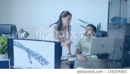 Pointing woman and seated coworker analyzing laptop and monitor rendering of robotic hand in office Pointing woman and seated coworker analyzing laptop and monitor rendering of robotic hand in office 139254881