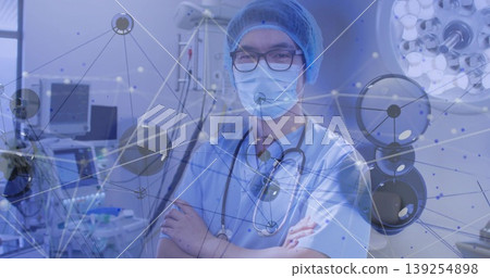 Standing Chinese doctor in scrubs in OR with stethoscope, monitor and pump under digital overlay 139254898