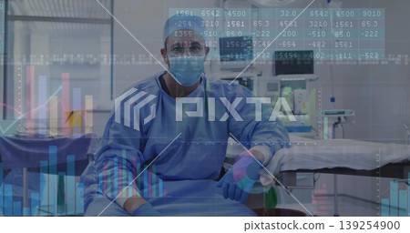 Sitting surgeon wearing blue scrubs mask at operating table in OR suite with trolley, data overlays Sitting surgeon wearing blue scrubs mask at operating table in OR suite with trolley, data overlays 139254900
