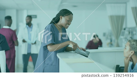 Pointing female nurse wearing navy scrubs consulting patient at reception desk, with tablet device 139254916